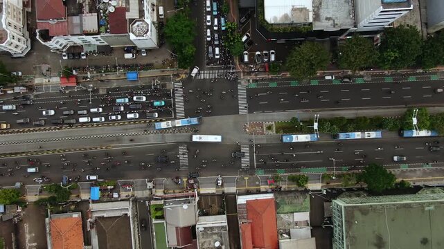 Aerial Top View of Busy City Crossroads with Traffic Flow and Buildings. High Angle Shot of Metropolitan Intersection featuring Cars, Motorcycles, City Bus, Zebra Crossings, and Green Bike Lanes