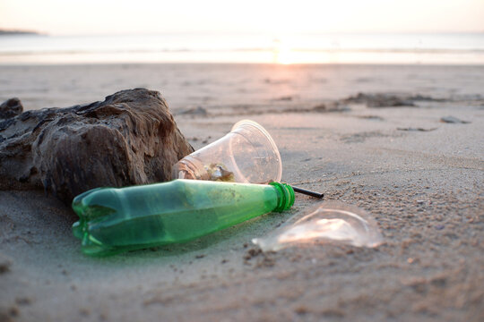Plastic bottle and cup litter on a beach at sunset, highlighting environmental pollution and its impact on nature