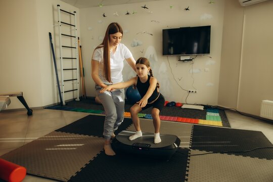 Therapist helping girl squatting on vibration plate therapy