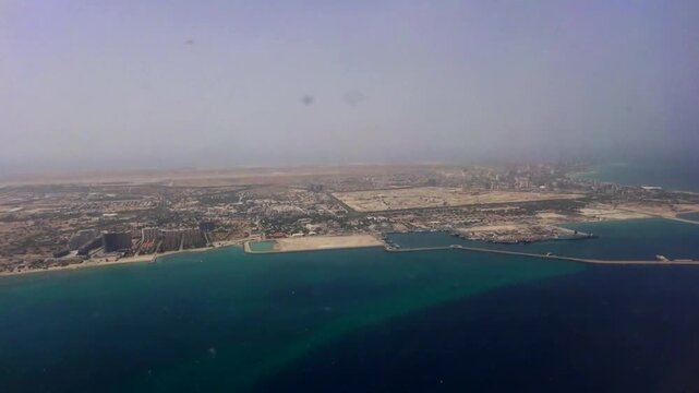 Coastal aerial of a bright seaside city fading into turquoise water, mixing warm hues of land and cool tones of ocean in a tranquil horizon view. 