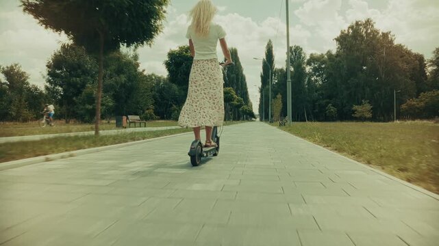 Riding Electric Scooter Along Paved Path In Park. Using Eco Friendly Transportation For City Trip. Sustainable Commuting Solution