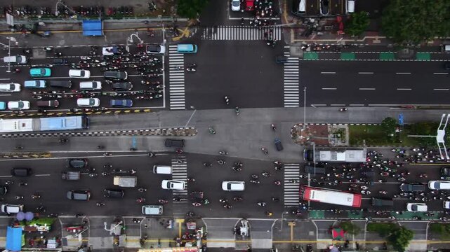 Aerial Top View of Busy City Intersection with Traffic Flow. High Angle Shot of Metropolitan Road featuring TransJakarta Buses, Motorcycles, Zebra Crossings, and Street Vendors on the Sidewalk