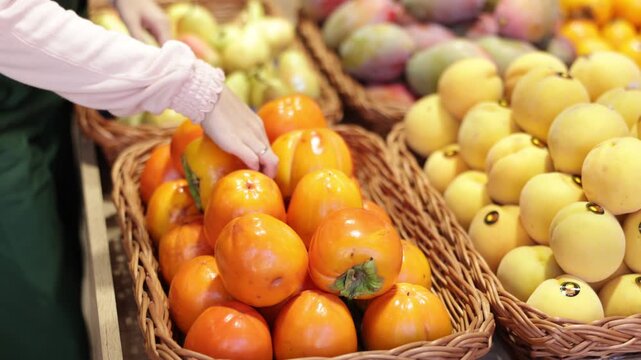 Hands of female seller puts fresh persimmon on counter of vegetable shop