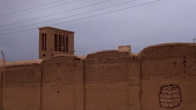  Massive adobe clay wall and ancient architecture of a historic Persian building, showing traditional construction materials, windcatcher and heritage site under sunlight. 