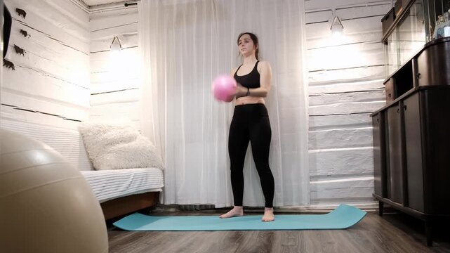 Caucasian woman playing and tossing up soccer ball up in the air and catches it with her hands on yoga mat at home. Girl wearing sportwear, black leggins and sports bra. Agility training. 4k footage.