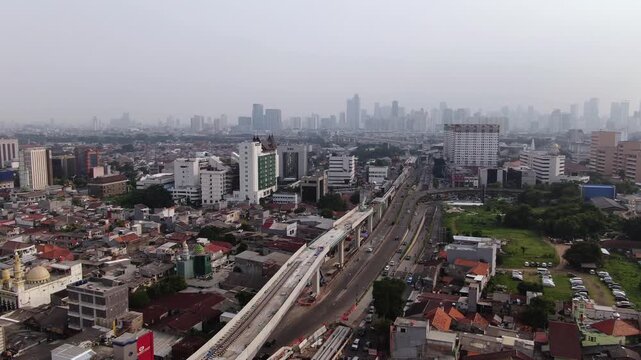 Aerial panoramic view of dense residential area with city skyscraper skyline background at sunset. High angle shot of urban infrastructure featuring elevated railway track and highway in metropolitan