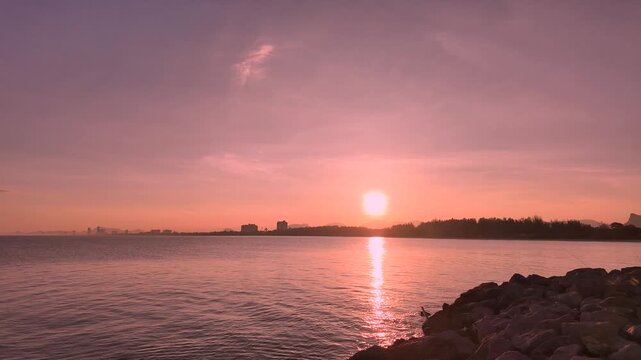 Sunset timelapse over calm sea with silhouettes of fishermen on Cha Am pier Thailand