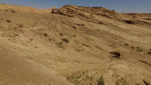  Sandy hillside descends through a dry desert terrain, featuring sparse scrub, eroded soil, and subtle geological textures that convey isolation and natural arid landforms under daylight. 