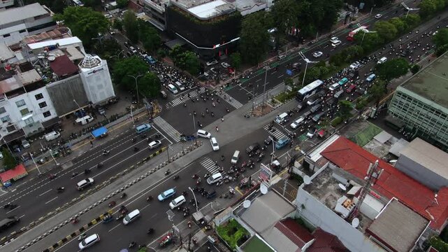 Aerial High Angle View of Busy City Intersection with Heavy Traffic. Featuring TransJakarta Buses, Cars, and Motorcycles Navigating Urban Roads Surrounded by Commercial Buildings and Metropolitan