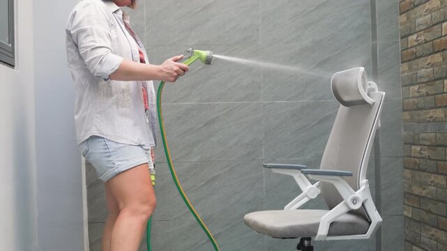 Modern home management involves using efficient tools to maintain a clean workspace. Woman sprays water on an ergonomic chair to keep furniture fresh. Approach to modern home management saves time