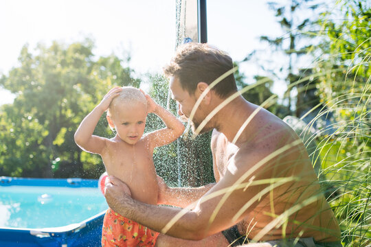 Son and dad using outdoor shower by the pool before swimming.