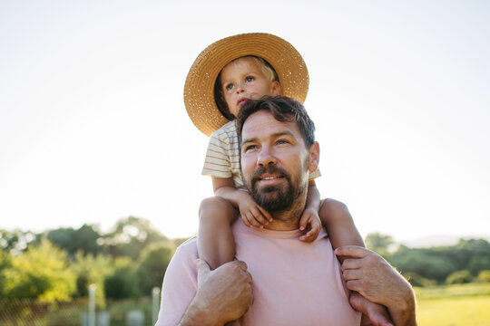 Dad carrying little boy on shoulders during warm summer day.