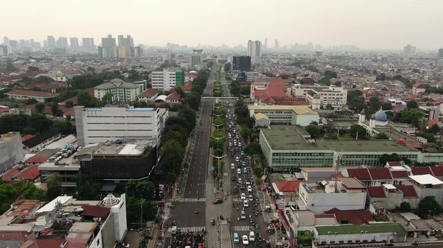 Aerial high angle view of a long city boulevard with traffic flow. Perspective shot of urban landscape featuring office buildings, a blue dome mosque, and skyscraper skyline under a hazy metropolitan