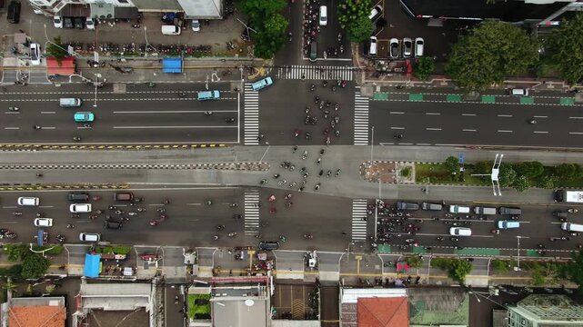 Aerial top down view of a busy city intersection. High angle shot featuring TransJakarta bus, green bicycle lanes, and heavy motorcycle traffic flow navigating the organized metropolitan road