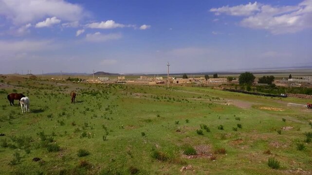 Rural valley with scattered houses, green fields and distant hills under open sky. Quiet countryside landscape shows human settlement blended into natural terrain during daylight. 