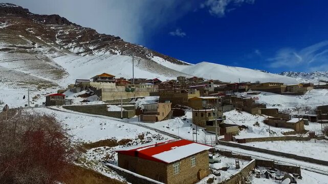  Mountain village surrounded by snow covered peaks and rooftops. Winter scenery combines human settlement with alpine landscape under bright blue sky daylight. 