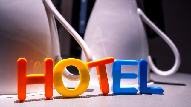 colorful toy letters spelling hotel placed in front of white ceramic mugs in a brightly lit indoor setting representing hospitality service and accommodation concepts for travelers