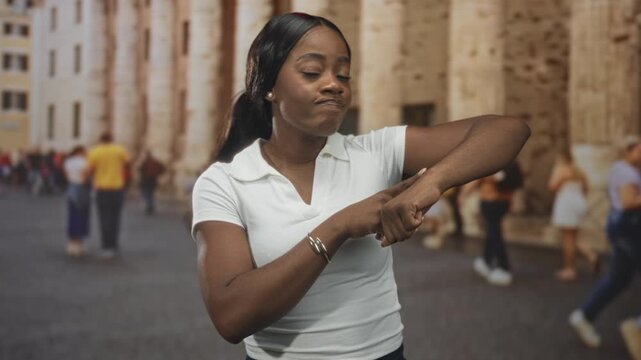 Woman checks wrist with a twisting arm gesture on a street lined with stone columns and blurred tourists; impatience travel.