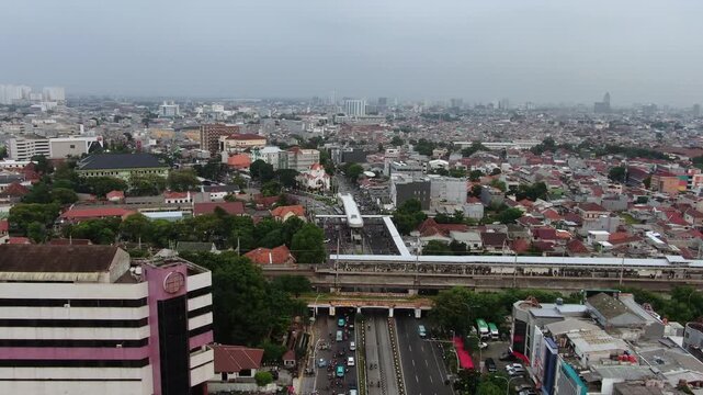 Aerial view of a commuter train station integrated with busy city roads. High angle shot of urban transit infrastructure, office buildings, and dense residential housing in a metropolitan