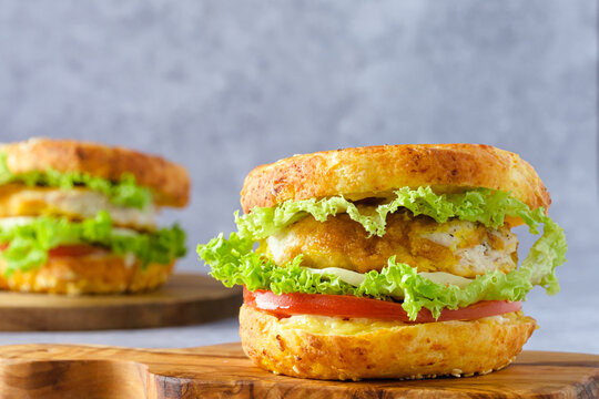Two bagel sandwiches on a cutting board, filled with crispy chicken, lettuce, and tomato on a gray background. Modern breakfast concept and healthy morning routine.