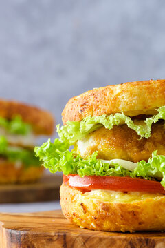  Close up bagel sandwiches on a cutting board, filled with crispy chicken, lettuce, and tomato on a gray background. Modern breakfast concept and healthy morning routine.