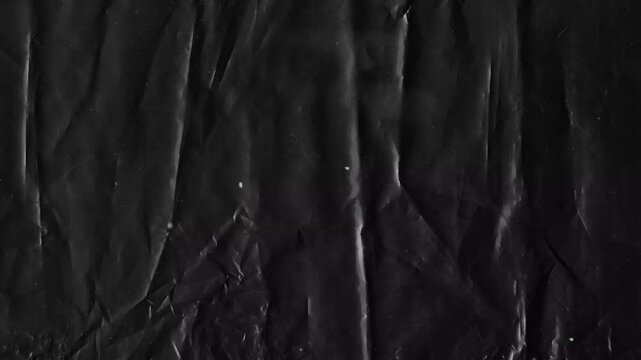 Black crumpled plastic texture background with subtle creases and light reflections animated background