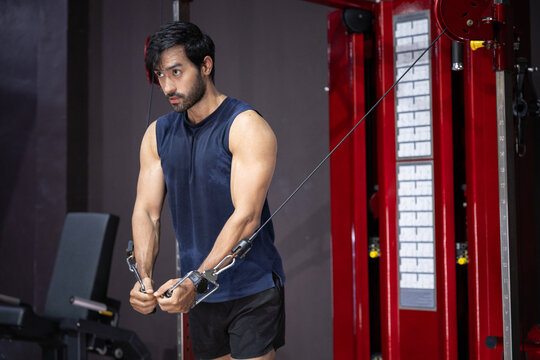 Gym workout man cable machine strength training triceps athletic fitness, focused athlete perform cable pushdown exercise with pulley machine indoor gym, muscular arms training for strength