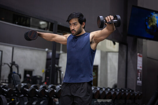 Man gym dumbbell workout strength training shoulder exercise fitness muscular focused indoor adult male doing dumbbell lateral raise modern gym, building strength and endurance with intense focus