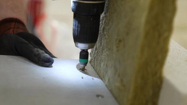Precision screw fastening for industrial firestop plates. Professional cordless drill assembly secures protective boards over mineral wool and masonry bricks for certified structural safety.
