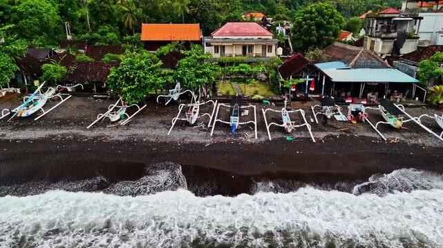 Aerial of a long row of white jukung outrigger boats on a black volcanic sand beach fronting Amed village. Amed, Bali, Indonesia, Perahu Jukung.