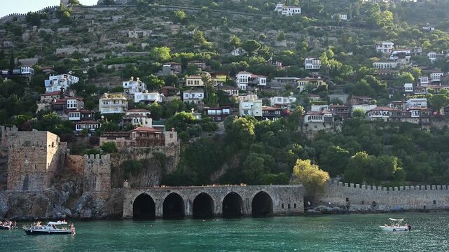 Beautiful view of modern yacht in front of medieval shipyard Tersane and Alanya Castl in Turkey. Historical Seljuk fortress on hill, turquoise Mediterranean sea and summer nautical travel concept