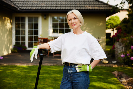 Mature woman resting on garden spade in backyard