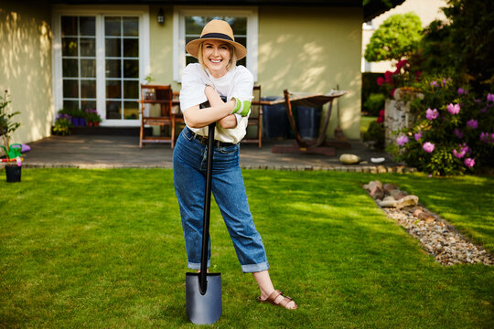 Mature woman leaning on shovel smiling in backyard garden