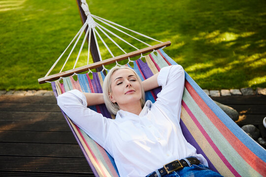 Mature woman resting in colorful hammock in backyard garden