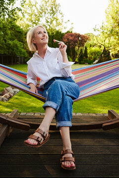 Mature woman relaxing in hammock eating watermelon in backyard