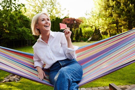 Mature woman eating watermelon on hammock in backyard