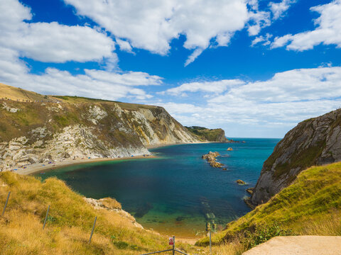 High angle view of a calm sea cove surrounded by steep rocky cliffs on a sunny summer day (Lulworth, England, United Kingdom)