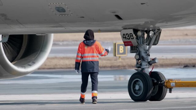 Airplane technician worker man landing gear runway. Airport terminal maintenance crew aircraft towing vehicle. Close-up of airplane's wheels.