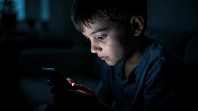 Young boy focused on smartphone screen in dark room using mobile device technology at night