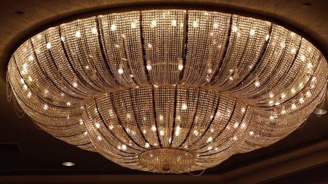 Golden chandelier hangs above elegant room. Crystal strands glow warmly from many lights. Each facet catches light with brilliance. Luxury radiates from ceiling fixture
