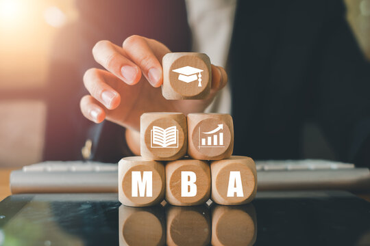 Close-up of a hand arranging wooden blocks with MBA-related icons, symbolizing education and business growth in a modern office.