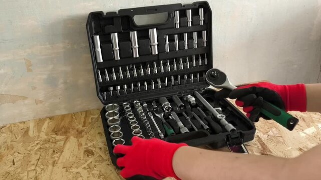 The hands of a repairman in red work gloves take a ratchet and a screwdriver attachment from a case with hand tools. Car repair shop, garage