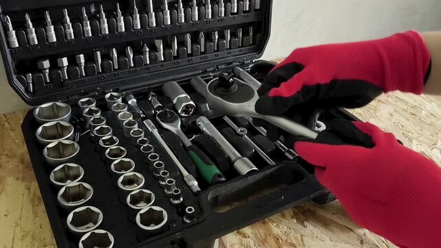 The hands of a repairman in red work gloves take a ratchet and a screwdriver attachment from a case with hand tools. Car repair shop, garage