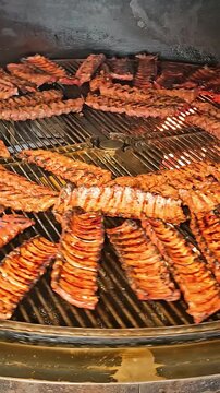 Barbecue ribs cooking on a circular smoker grill. A large circular smoker grill filled with rows of barbecue ribs sizzling over a fire.