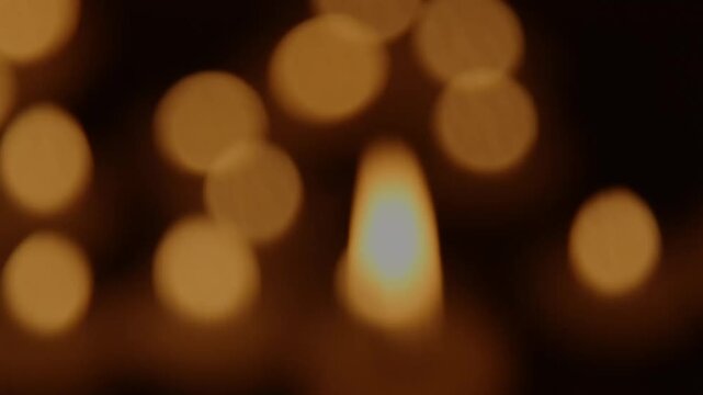 Burning candle flame moves gently against warm golden bokeh lights indoors, then the image gradually darkens toward the end, showing calm motion, fading light, and a memorial holiday concept.
