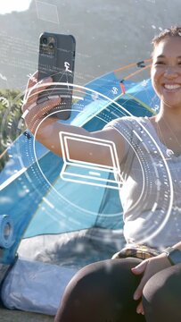 Vertical video: Camper raising phone starting AR fintech HUD showing money icons for managing funds