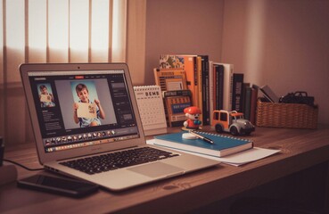 Obraz premium A cozy workspace with a laptop displaying a child's photo, surrounded by books, stationery, and playful elements.