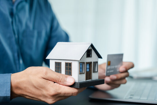Real estate and mortgage concept. Person holding model house and credit card.