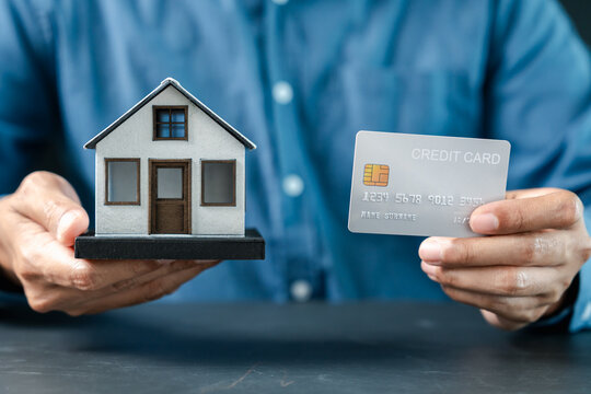 Real estate and mortgage concept. Person holding model house and credit card.