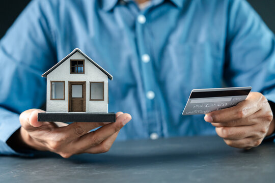 Real estate and mortgage concept. Person holding model house and credit card.